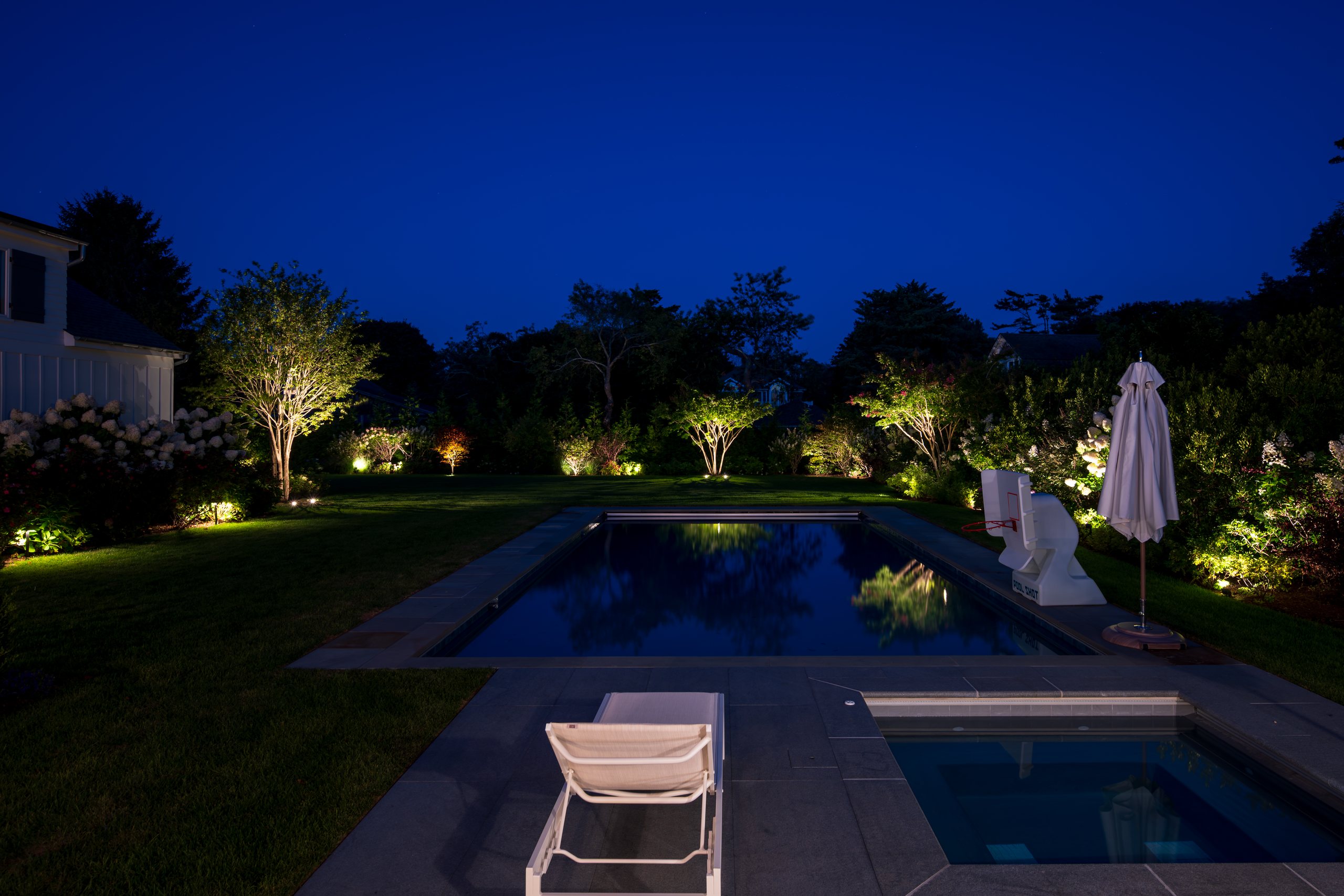 Long Island outdoor lighting around a backyard pool and landscape after sunset